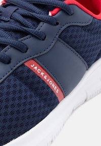 Αθλητικό παπούτσι σε ναυτικό μπλε χρώμα με ύφασμα από δίχτυ, μπλε κορδόνια, κόκκινη εσωτερική επένδυση, λευκή σόλα κα ι κόκκινη ετικέτα με λευκή επιγραφή "JACK & JONES".