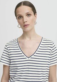 T-shirt a righe con scollatura a V in crema con strisce blu navy. Tessuto morbido, maniche corte, presenta un orlo pulito e una vestibilità rilassata.