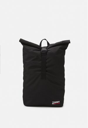 Mochila negra tipo roll-top hecha de un tejido duradero, que presenta un cierre de hebilla robusta y un pequeño logo en la esquina inferior.