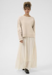 Beige bavlněná mikina s vyšitým vzorem na rukávech, doplněná lehkou, průsvitnou krémovou skládací maxi sukni a černými botami.