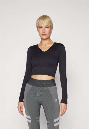 Musta pitkähihaiset crop-top V-pääntiellä, yhdistettynä harmaisiin kuviollisiin legginsseihin, joissa on ribbimäinen rakenne ja raidallinen yksityiskohta.
