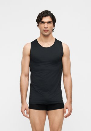 Jeune homme aux cheveux courts et foncés, vêtu d'un débardeur noir ajusté sans manches et d'un short noir, face à un fond uni.