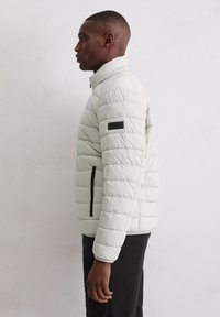 Kurtka puchowa w jasnym kolorze z poziomym pikowaniem, wyposażona w czarne zamki błyskawiczne, kieszeń boczną na zamek oraz stójkę.