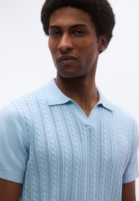 Ανοιχτό μπλε πλεκτό πόλο πουκάμισο με υφασμένους ανάγλυφους σχεδιασμούς καλωδίου, μανίκια κοντά και μαλακ ό σχεδιασμό γιακά.