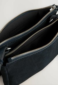Sort suede-pung med to lynlåse, sølvfarvede metal lynlåse og et glat indre for. Kompakt design med rektangulær form.