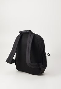 Mochila negra con textura de malla, forma contorneada, correas de hombro acolchadas y un asa superior. Cuenta con correas laterales ajustables para un cierre seguro.