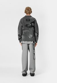 Suéter gris de punto con patrones abstractos, con cuello redondo y puños acanalados. Combinado con pantalones deportivos grises y calzado negro.