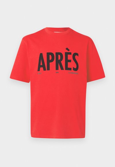 Κόκκινη κοντομάνικη μπλούζα τύπου crewneck με μεγάλο μαύρο κείμενο "APRÈS" και μικρότερες λέξεις "GOLF," "SKI," και "J.LINDEBERG" κάτω από το κέντρο μπροστά.