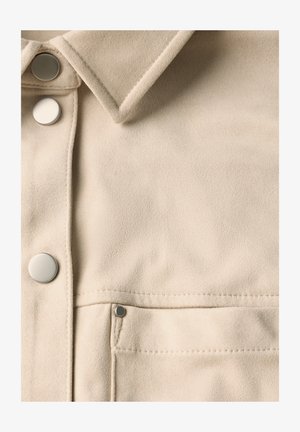 Beige Wildlederjacke mit spitzem Kragen, silbernen Druckknöpfen und einer Brusttasche. Weiche Textur mit minimalen Nähten.