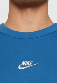 Blå bomullströja med rundad halsringning och korta ärmar. Har en vit broderad Nike-logga på framsidan.