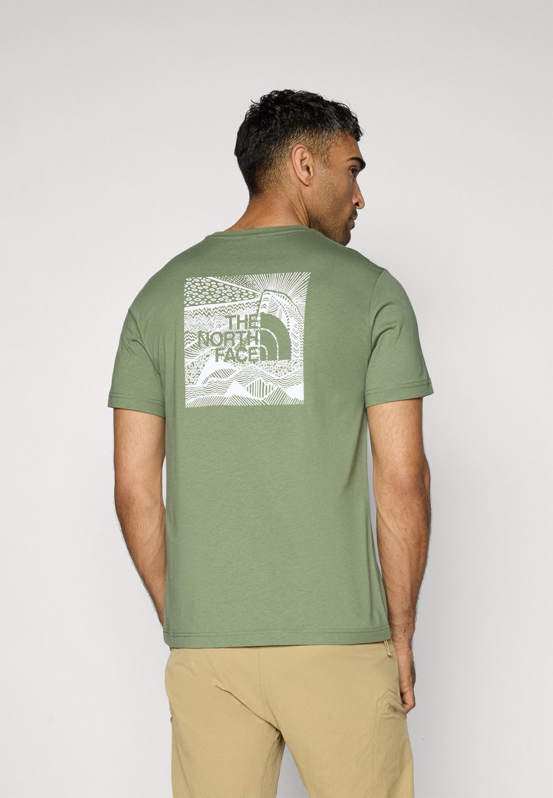 Camiseta de algodón verde con mangas cortas, con un estampado gráfico blanco en la parte posterior de montañas y el logo de "The North Face".