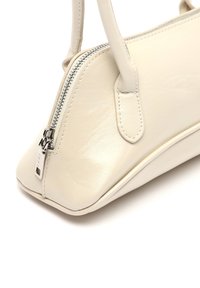 Borsa a mano in pelle beige chiaro con design strutturato, base inclinata, manici corti e dettagli con zip in tonalità argento. Texture liscia, senza motivi.