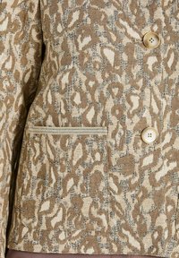 Braun- und cremefarbener, strukturiertes Jackett mit einem abstrakten Leopardenmuster, zwei beige Knöpfen und einer Paspeltasche auf der Vorderseite.