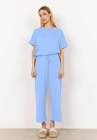 Ljusblå matchande set som består av en avslappnad topp med kort ärm och byxor med vid ben och snörning. Materialet verkar mjukt med minimal textur.