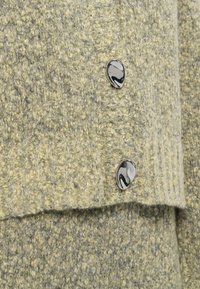 Knit sweater in light gray and yellow with a textured pattern, featuring two glossy, black-and-white marble buttons.