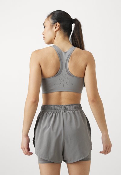 Sostén deportivo gris con diseño de espalda deportiva y sutiles acentos en puntos; combinado con pantalones cortos grises de corte holgado y cinturilla elástica.