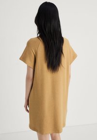 Rochie supradimensionată cu mânecă scurtă, de culoare mustar cald, cu o textură moale, având o croială lejeră și un tiv rotunjit.