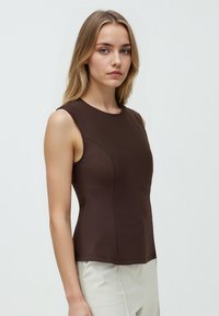 Top marrone senza maniche realizzato in tessuto elastico, caratterizzato da una silhouette aderente e cuciture pulite, abbinato a pantaloni chiari.