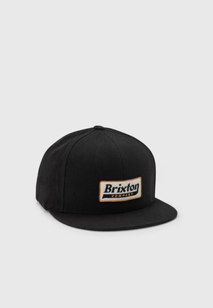 Czarna czapka z płaskim daszkiem, z prostokątną naszywką z przodu z napisem "Brixton Company" czarnymi i pomarańczowymi literami.