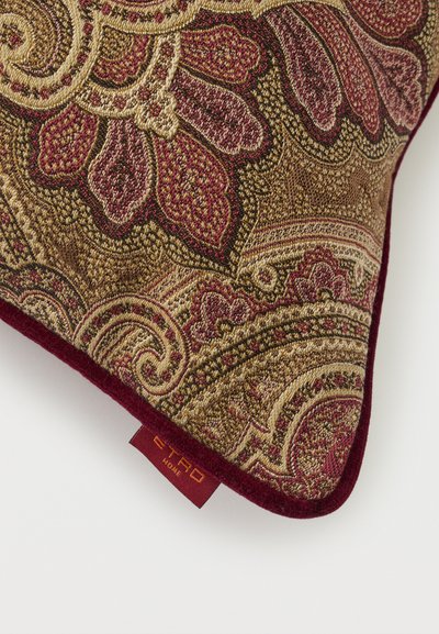 Coin de coussin décoratif avec un motif paisley détaillé bordeaux et or et une petite étiquette en tissu rouge portant l'inscription "ETRO HOME".