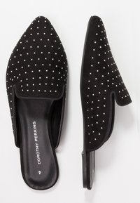 Svart mockaklackskor med spetsig tå och nitar som dekoration. Texturerad yta med platt sula och en rundad, öppen häll.