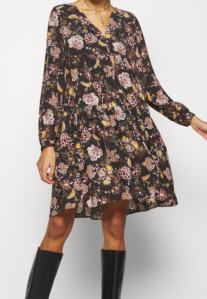 Schwarzes Blumenkleid mit langen Ärmeln, V-Ausschnitt und gerafftem Taillenteil. Der Stoff hat eine weiche, strukturierte Oberfläche mit mehrfarbigen Blumenmustern.