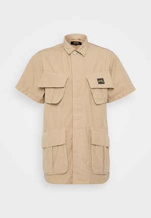 Short-sleeve, light tan shirt made of cotton with a button-up front, two chest pockets, and two lower pockets. Features a branded label.