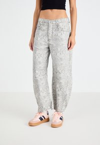 Grijs en witte slangenhuidpatroon wijdvallende jeans met een hoge taille, voorzien van zakken en subtiele stikdetails, gecombineerd met lichtroze sneakers.