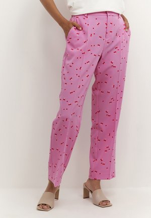 Person wearing high-waisted pink pants with small red cherry print, paired with beige open-toe block heel mules.