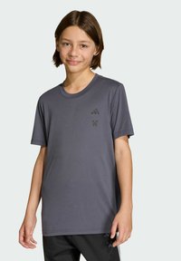 Šedé športové tričko s krátkymi rukávmi, okrúhlym výstrihom a tónovým logom Adidas na hrudi. Hladká, ľahká tkanina; pravidelný strih.