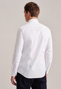 Witte blouse met lange mouwen en een puntige kraag, met een gladde textuur en een gespleten achterkantnaad. Knopmanchetten met subtiele details.