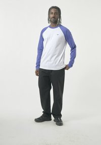 Langarm-Raglan-Shirt in Weiß und Lila mit Rundhalsausschnitt. Schwarze Hose und schwarze Schuhe. Einfaches Design, lässige Passform.