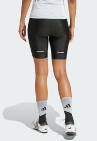 Black cycling shorts with a padded seat, featuring reflective stripes, paired with grey and black sport socks, and white athletic shoes.