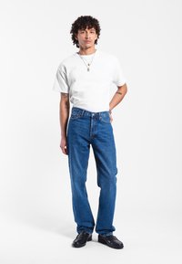 Camiseta blanca de algodón combinada con jeans de mezclilla azul de tiro alto. Los jeans presentan un corte recto, costuras sutiles y un diseño clásico de cinco bolsillos.
