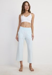 Pantaloni lounge a vita alta di colore azzurro chiaro, tagliati in lunghezza, con una cintura elastica ampia e un motivo a pois delicato. Indossati con un semplice bralette bianco.