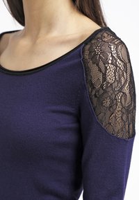 Lila Pullover mit einer taillierten Passform und weitem Ausschnitt. Verfügt über schwarze Spitzenakzente an den Schultern, die Textur und Kontrast bieten.