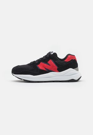 Black and red sneakers feature a suede and mesh upper, a white midsole, and a textured black sole, with a prominent red logo detail.