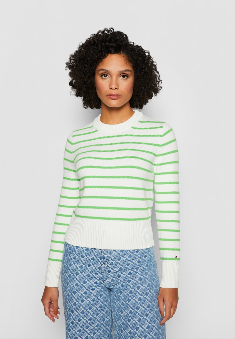 Weiß gestreifter Pullover mit grünen horizontalen Streifen, geripptem Saum und Bündchen. Getragen mit gemusterten hellblauen Jeans mit geometrischem Design.