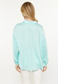 Lichtblauwe zijden shirt met een kraag, drop shoulders en ballonmouwen. De achterkant heeft een afgeronde zoom en een gladde textuur.
