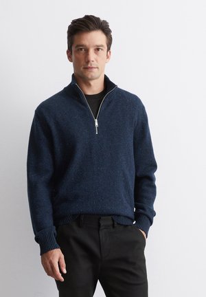 Navy blue, textured knit pullover sweater with a zip collar and ribbed cuffs, paired with black trousers. Simple design and casual fit.