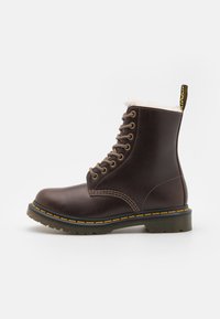 Bottines en cuir marron à lacets, avec une doublure en fausse fourrure blanche, des coutures jaunes et une semelle noire texturée. Présente un onglet jaune à l'arrière.