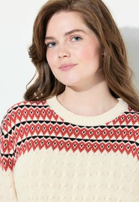 Maglione lavorato a maglia con una base color crema, un giogo pattern rosso e nero, collo rotondo e tessuto testurizzato.
