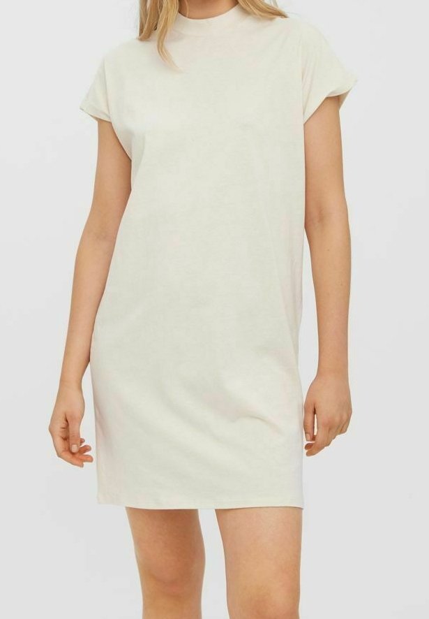Femme portant une robe crème unie, à manches courtes, longueur genoux, avec un col rond, sur un fond neutre.