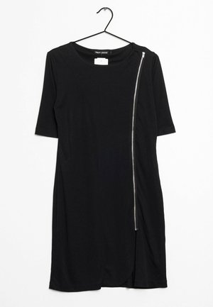 Zwarte jurk tot op de knie met ellebooglange mouwen en een zilveren asymmetrische ritssluiting die loopt van schouder tot zoom, hangend aan een zwarte hanger.