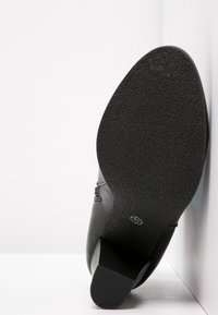Black leather shoe with a textured rubber sole, featuring a slightly raised heel and minimalist design. Side profile shows smooth lines.