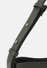 Olijfgroene leren handtasband met een gladde textuur, voorzien van zilveren metalen studs en een zwarte rand voor contrast.