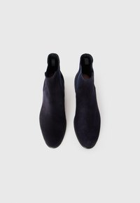 Par de botas Chelsea de camurça azul-escuro com painéis laterais elásticos e puxadores, mostradas de cima sobre um fundo branco.