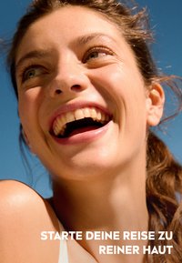 Close-up of a smiling woman with clear skin, brown hair, and wearing a light strap top, set against a bright blue sky. Text below reads in German.