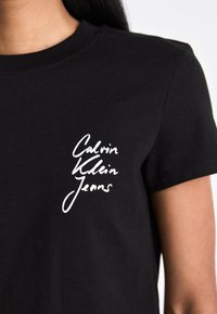 Camiseta negra de algodón, con un logo impreso en blanco "Calvin Klein Jeans" en el lado izquierdo del pecho y un corte casual.