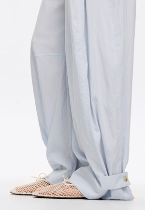 Lichtblauwe, losse broek met aangeknoopte onderkanten, gecombineerd met witte mesh ballerina's met een knoopdetail en platte zolen.